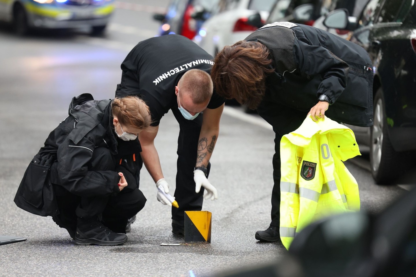 Kriminaltechniker untersuchen und markieren ein auf dem Boden liegendes Projektil am Tatort in Wuppertal.