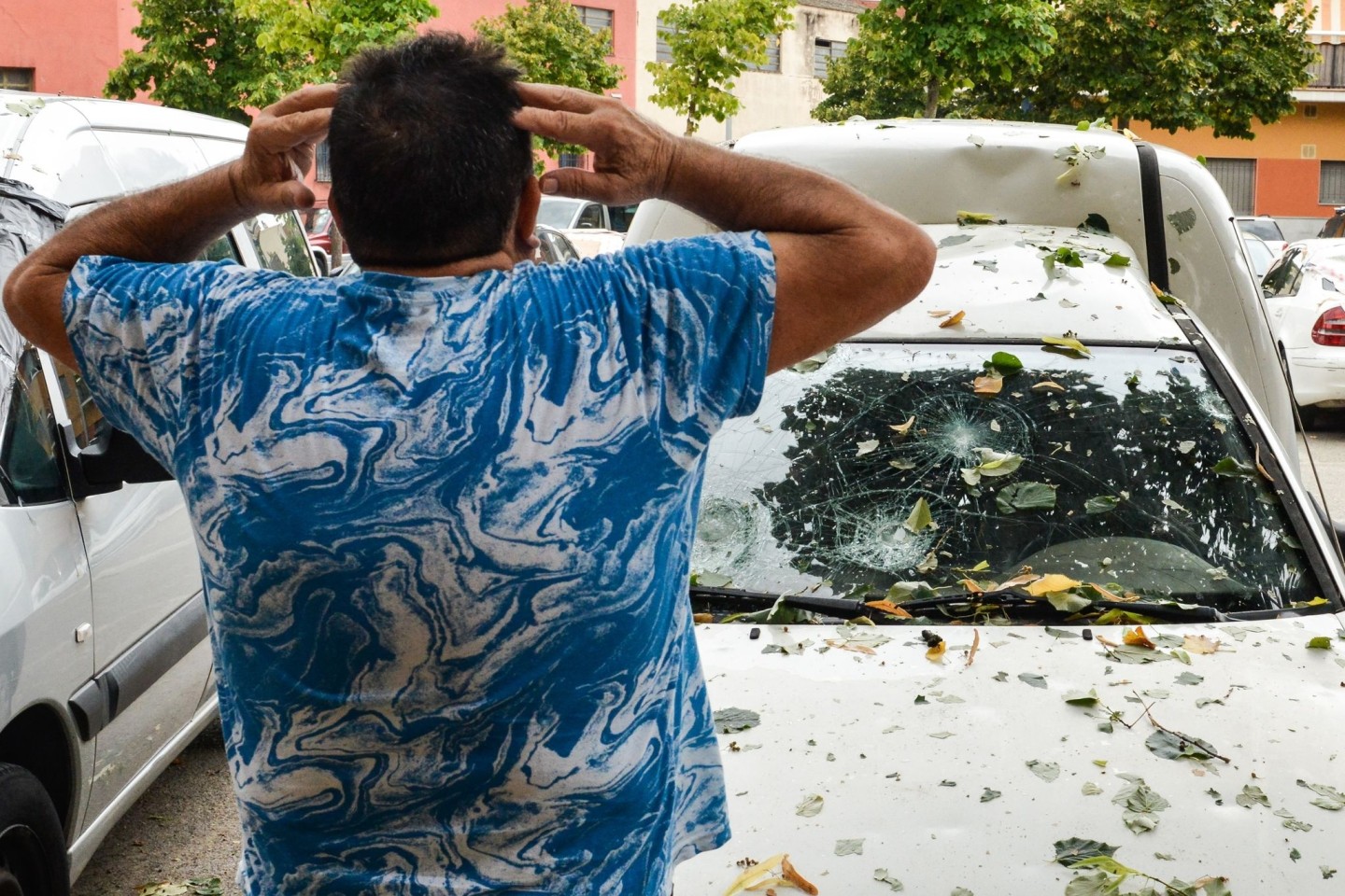 Ein Mann hält sich die Hände an den Kopf, als er die Schäden an seinem Auto nach einem Hagelsturm sieht.