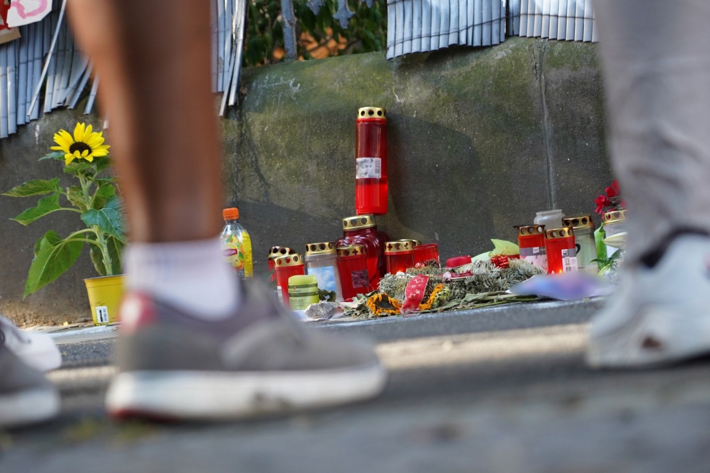 Menschen stehen vor einem Zaun, an dem mit Kerzen und Blumen eines von der Polizei erschossenen Jugendlichen gedacht wird.